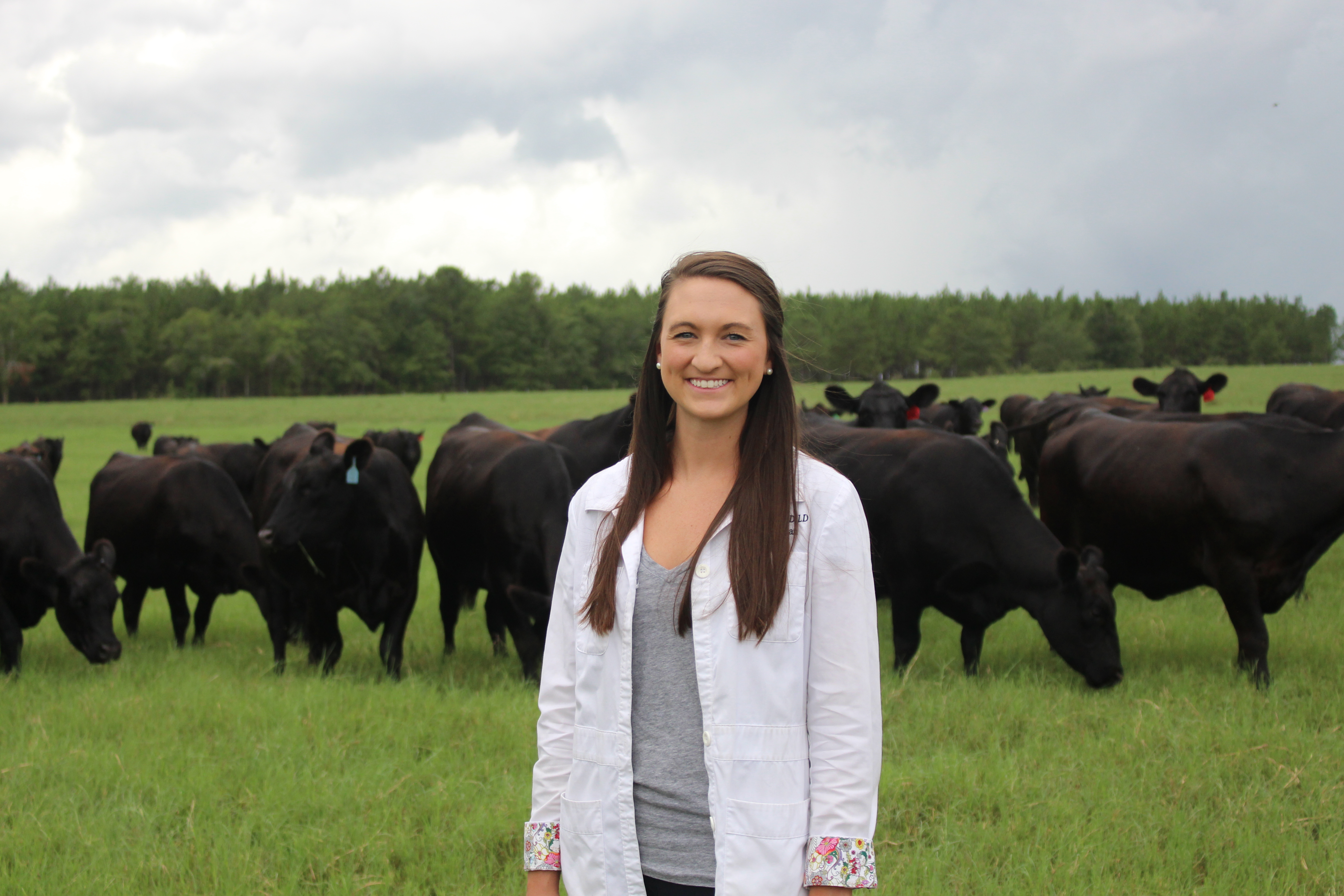 Woman in lab coat posing by herd of cows